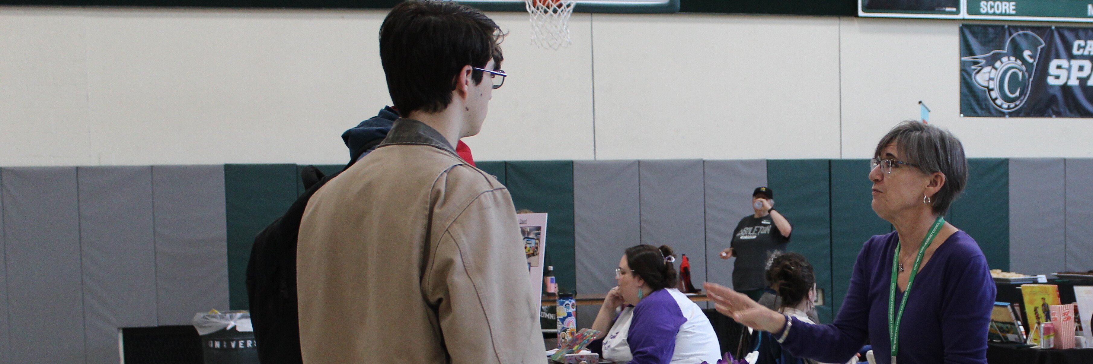 a woman talking to two men in a gymnasium- career fair set up