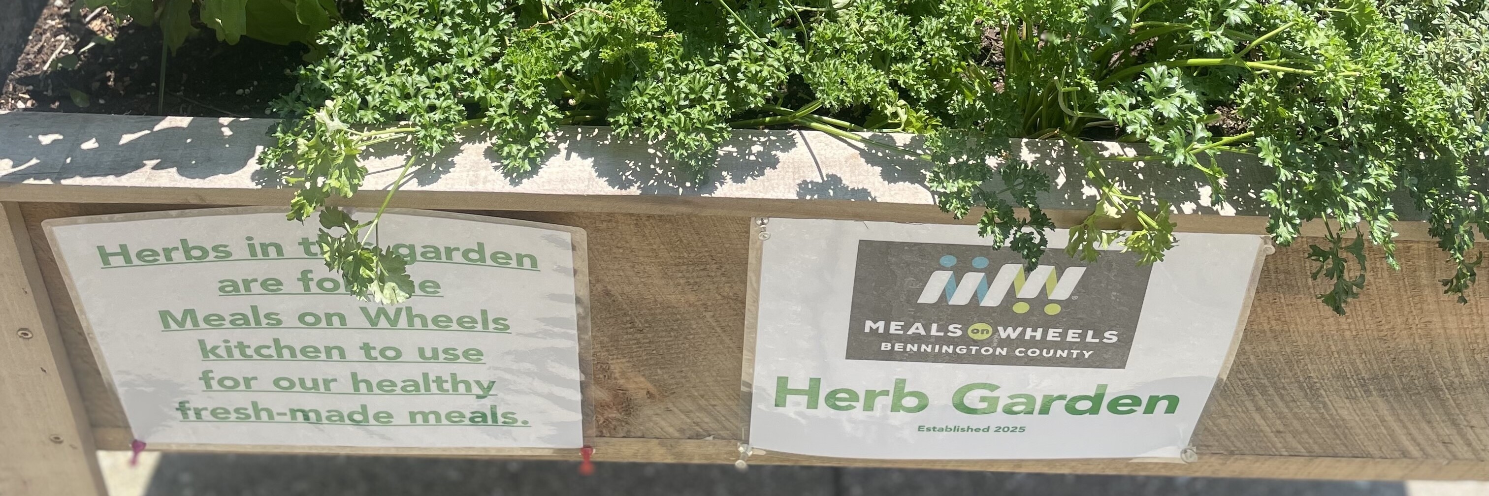 a herb garden in an upright wood planter with a sign saying Meals on Wheels Bennington County Herb Garden
