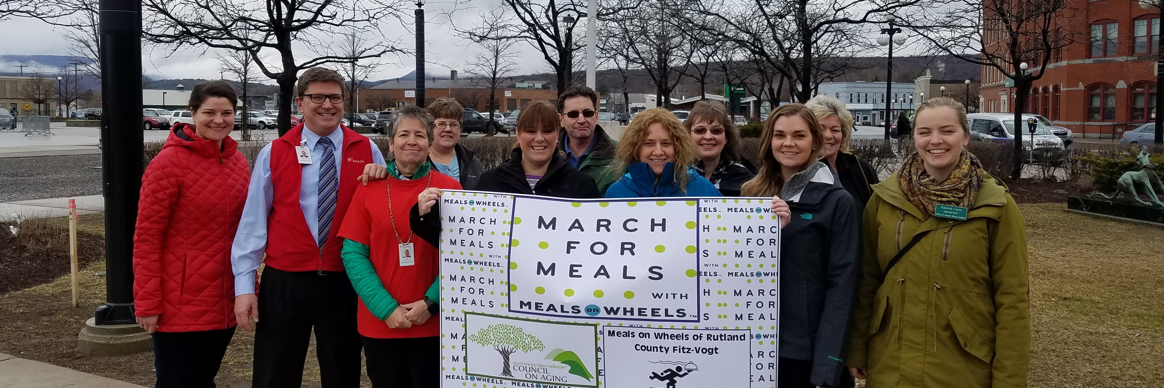 group smiling with march for meals on wheels sign